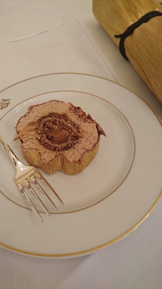 La bûche Noisette: chocolat brossé à l'or, gâteau roulé noisette, coeur tendre caramel, mousse noisette, nœud croquant au chocolat.